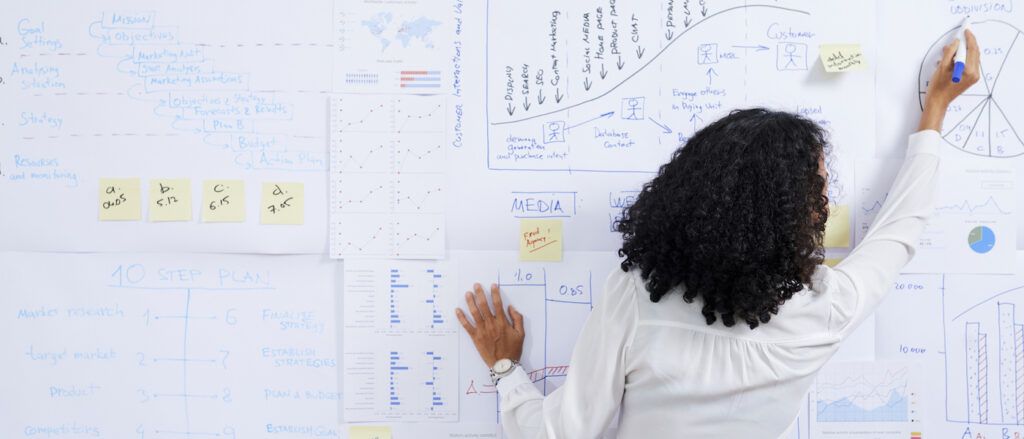 Businesswoman with curly hair drawing diagram on whiteboard when preparing for data-driven marketing presentation