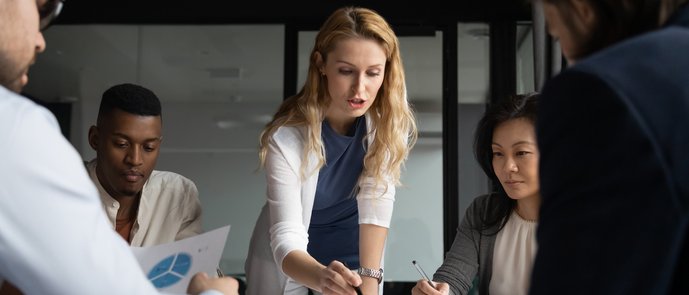 Concentrated young businesswoman explaining market research results in graphs to mixed race colleagues.