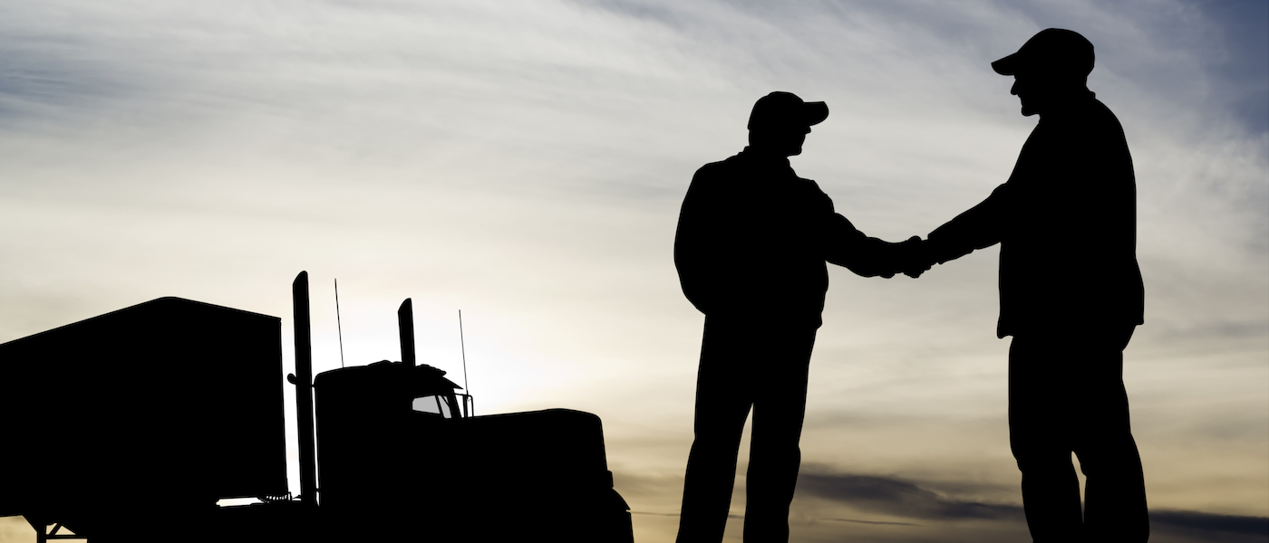 two men shaking hands with a long-haul truck in the background