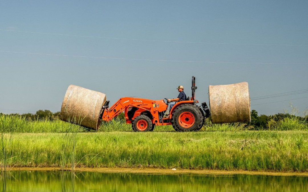 man on tractor with bails of hay along river