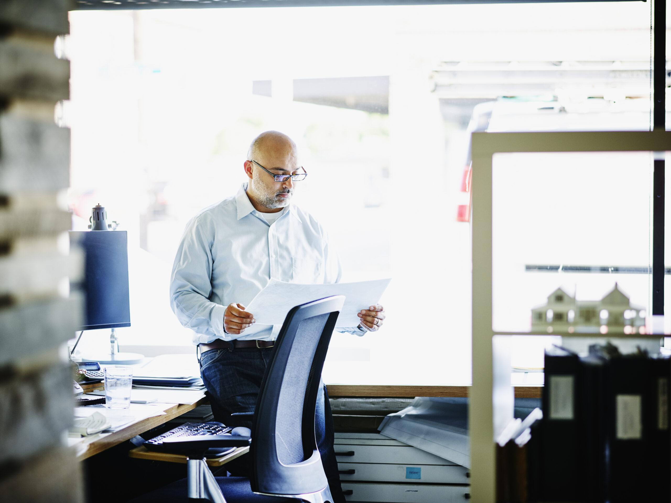 Small business owner leaning on desk at office workstation looking over project plans