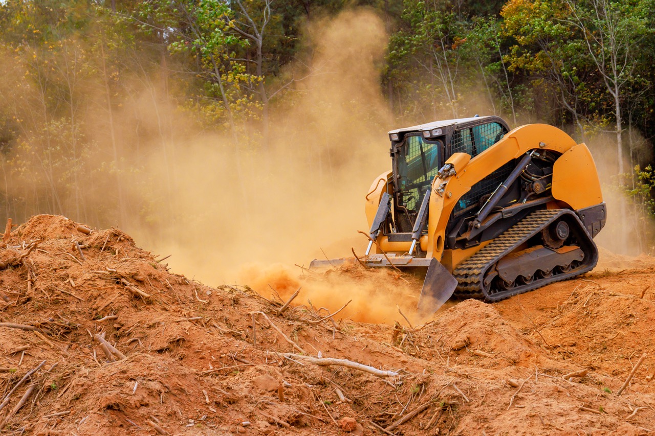 Orange tracked bulldozer in operation, kicking up a dusty orange cloud while moving soil on a construction site.