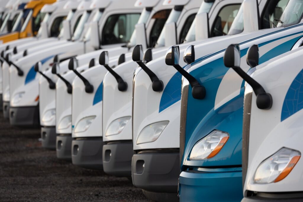 Row of white and blue semi-trucks parked in a line, nose-to-nose, in a fleet yard