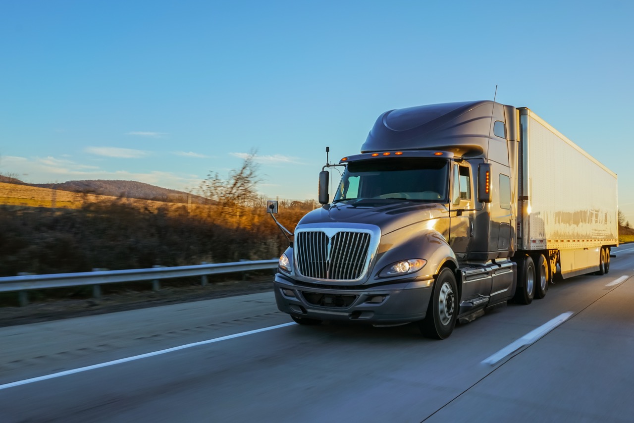 Silver semi-truck with a large white trailer driving on a highway at golden hour.