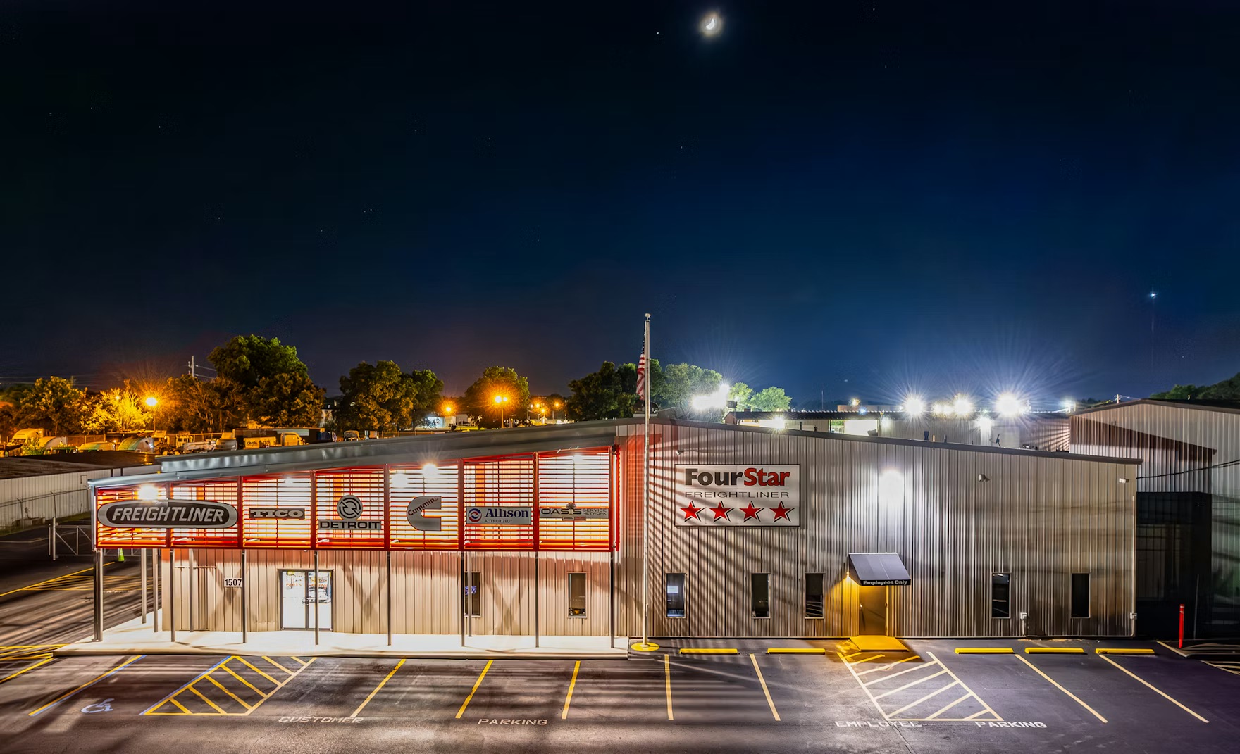 Night exterior of a freight service building with 'FourStar' and 'Freightliner' signage, illuminated parking lot beyond.