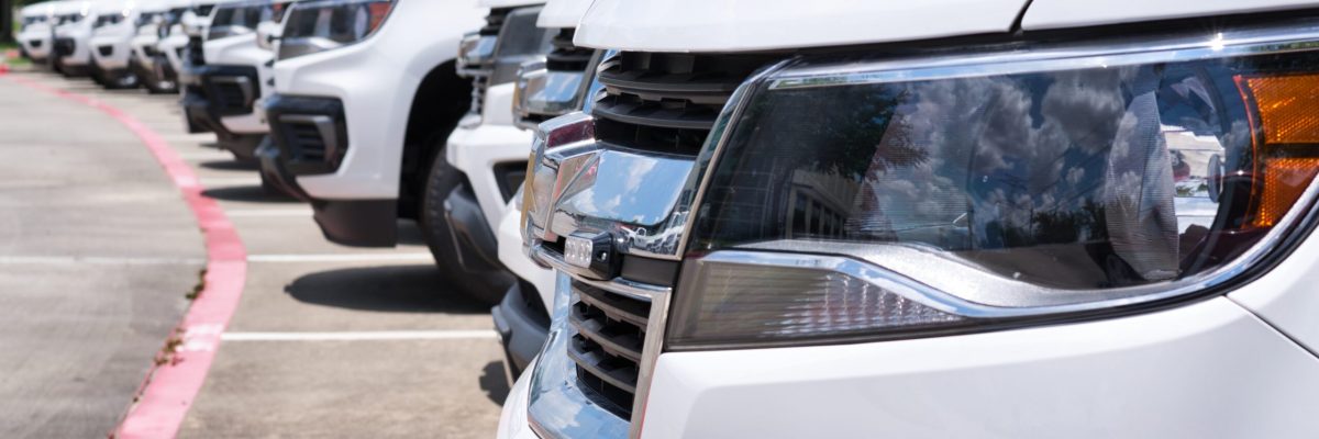 White generic fleet SUV's parked in a lot, side closeup on front of vehicle with focus on foreground. Transportation and logistics industry.